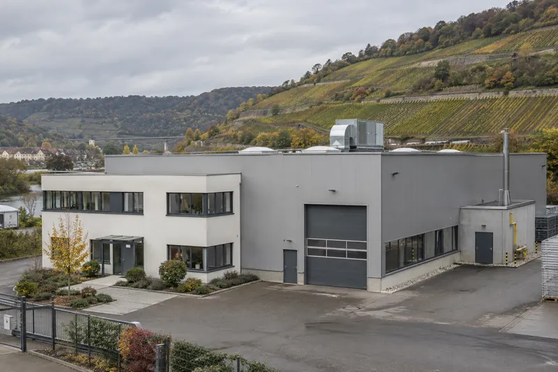 Zuliefererhalle mit Bürotrakt im Neckartal, im Hintergrund Weinberghang, auf dem Flachdach ein Lüftungsgerät