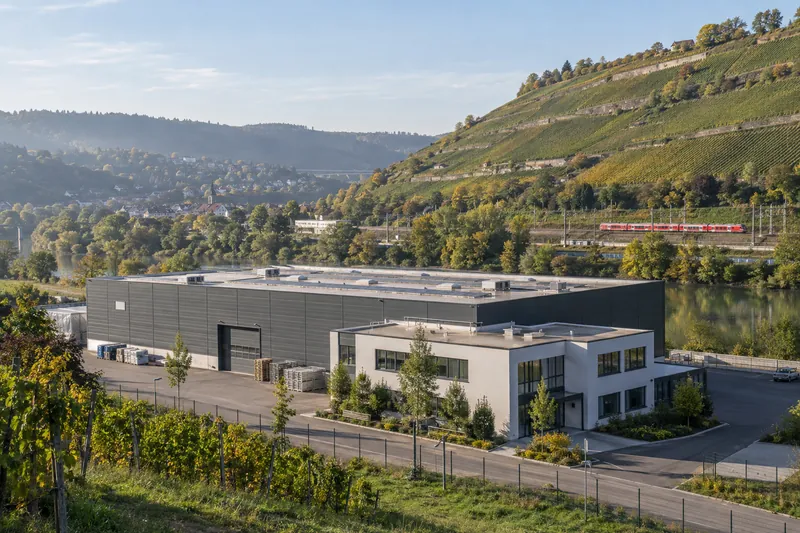Moderne Produktionshalle mit Büroanbau im Neckartal, dahinter Weinberghänge bei Stuttgart