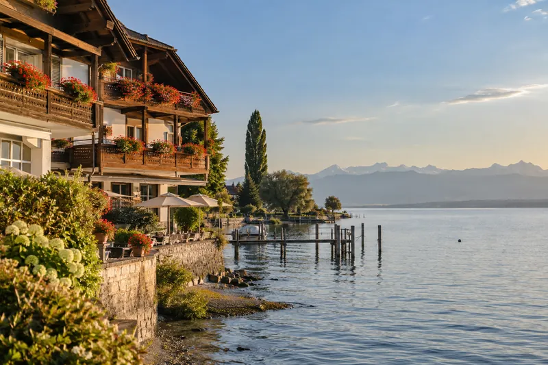 Familiengeführtes Hotel mit Holzbalkonen am Bodensee, im Hintergrund Wasser und Alpenkette