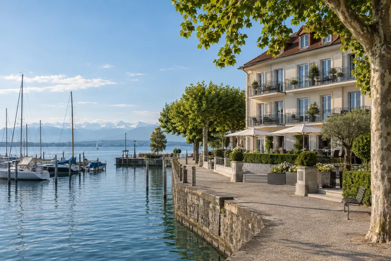 Saniertes Hotelgebäude am Bodensee mit Balkonen, Hafen und Alpenkette im Hintergrund