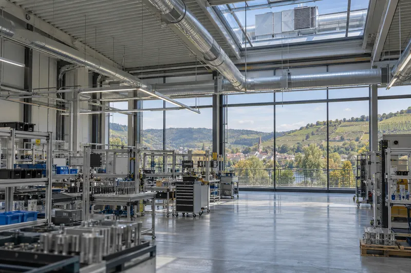 Lichte Fertigungshalle mit sichtbaren Lüftungskanälen, im Hintergrund Weinberge im Neckartal