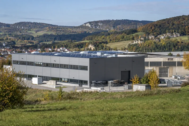Sanierte Produktionshalle mit neuer Fassade und Solardach neben einer unsanierten Halle am Rand einer Stadt auf der Schwäbischen Alb