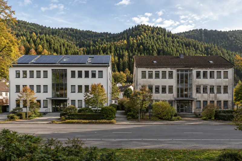 Zwei gleich geschnittene Gewerbehäuser nebeneinander, eines saniert mit Solardach, am Rand einer Schwarzwaldstadt