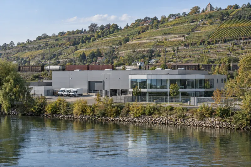 Gewerbehalle mit Büroanbau am Neckarufer, im Hintergrund Weinberghänge