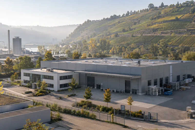 Gewerbehalle mit Büroanbau im Neckartal, dahinter Weinbergterrassen