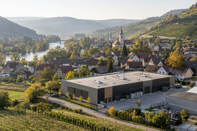 Moderne Produktionshalle im Neckartal mit Weinbergen und Fachwerkdorf im Hintergrund
