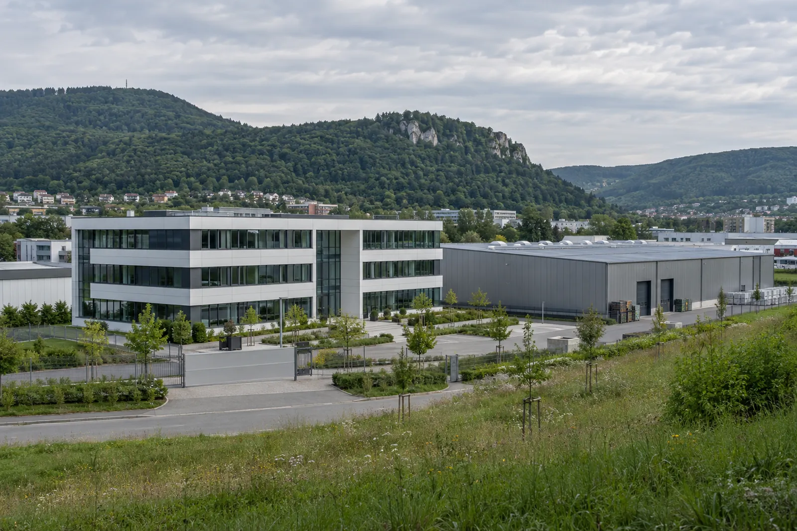 Gewerbebauten im Kochertal bei Aalen mit Bürogebäude, Hallenfassade und bewaldeten Höhen der Ostalb im Hintergrund