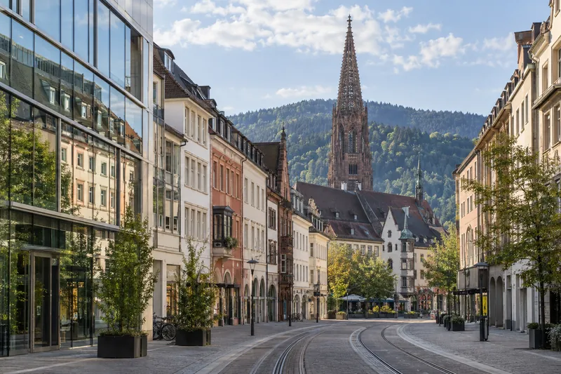 Geschäftshäuser in Freiburger Altstadt mit Münsterturm und Schwarzwaldhöhen im Hintergrund