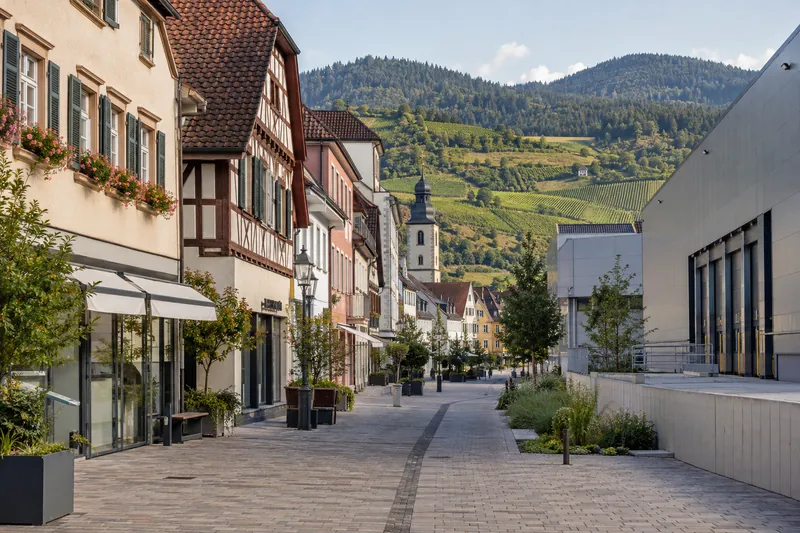 Geschäftshäuser mit Altstadtfassaden und Gewerbehalle vor Weinbergen im Schwarzwaldvorland