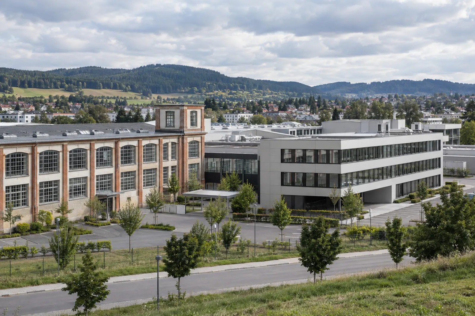 Ehemaliges Fabrikgebäude neben modernem Bürogebäude, im Hintergrund Hügel der Baar